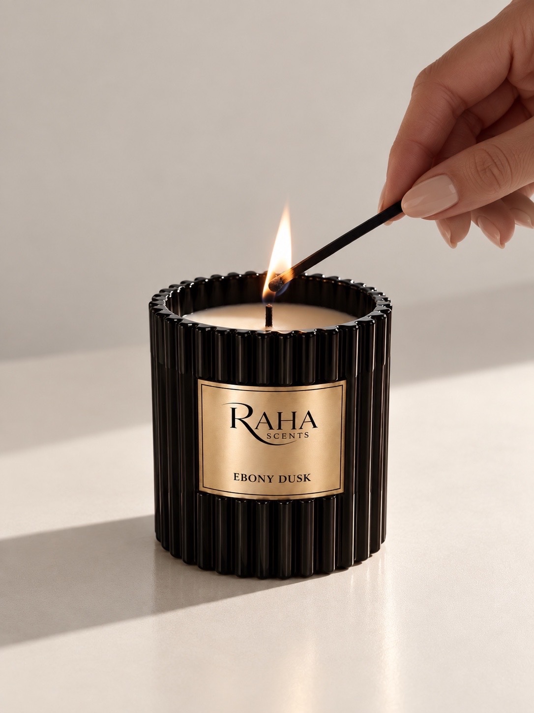 Raha Scents Ebony Dusk candle being lit in a softly lit interior